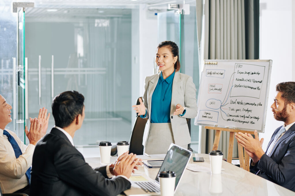 Businessmen clapping at a young corporate professional after her presentation.